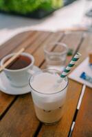 Glass of cappuccino with a striped straw stands on a wooden table next to a cup of tea photo