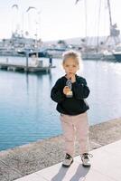 Little girl drinks juice through a straw from a bottle while standing on the boardwalk photo