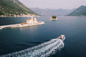 Yacht sails on the sea past the island of Gospa od Skrpjela to the island of St. George. Montenegro. Drone photo