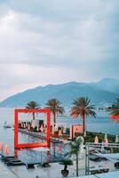 Illuminated red square arch stands in a long pool by the sea. Porto, Montenegro photo