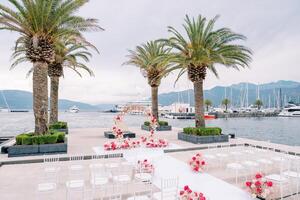 Round wedding arch stands on a pier with moored yachts in front of rows of white chairs photo