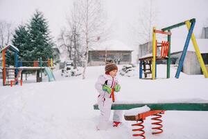 Little girl swing on a snow-covered swing-balancer at the playground photo