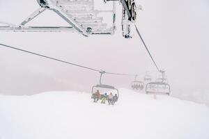 Four-seater chairlift with tourists moves through the fog up the mountainside photo