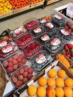 Budva, Montenegro - 25 december 2022. Fresh lychee berries, peaches, currents, raspberry blueberries in boxes lie on the counter photo