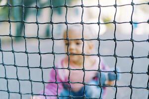 Little girl with a toy sat down behind the net. Blur photo