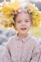 pequeño alegremente sonriente niña vistiendo un guirnalda de amarillo hojas. retrato foto