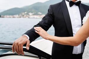 Bride touches groom hand while standing in a boat floating on the sea. Cropped. Faceless photo