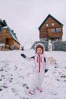 Little smiling girl walks along a snowy hill, waving her hand and looking down at her feet photo