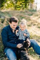 Dad sits on the lawn with his little daughter and strokes the dog photo