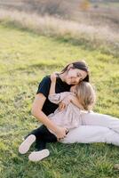 sonriente madre sentado en un verde césped abrazando su pequeño hija foto