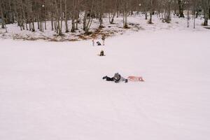 Young woman fell off the sled and lies on her stomach in the snow, looking away photo