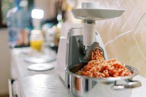 eléctrico carne amoladora giros carne dentro un pan en un cocina mesa foto