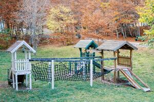 Wooden playground in the autumn forest with slides and agility mesh bridge photo