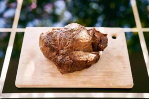 Roast beef on a cutting board lies on a glass table in the sunlight. Top view photo