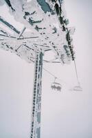 Snow-covered pillar of a four-seater chairlift with moving chairs photo