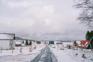 autopista mediante un cubierto de nieve pueblo con vistoso casas en un montaña Valle foto