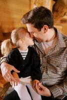 Dad hugs a little girl sitting on his lap, touching her cheek with his nose photo