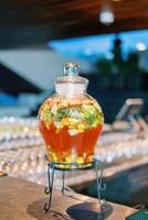 Red lemonade with pieces of fruit in a glass jar with a lid on a stand stands on the table photo