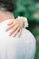 Bride hand hugs groom shoulder. Back view. Cropped photo