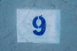 Number nine drawn on a scratched blue wall in a white rectangle photo