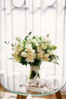 Bridal bouquet stands on a glass table in a room photo