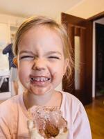 pequeño sonriente niña con un sucio cara sostiene chocolate hielo crema en un gofre taza foto