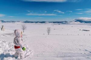 Little girl stands in a deep snowdrift in a mountain valley and looks into the distance. Side view photo