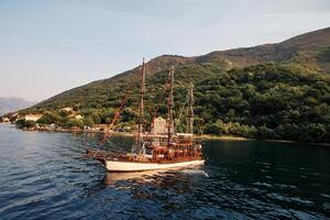 Wooden schooner sails on the sea against the background of a mountainous coast. Drone photo