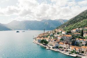 Ancient houses with red roofs on the shore of the Bay of Kotor at the foot of the mountains. Perast, Montenegro. Drone photo