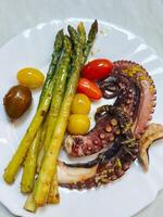 Fried octopus tentacles with asparagus and tomatoes lies on a plate photo