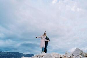 Man helps woman walk on the rocks, holding her hand in the mountains photo