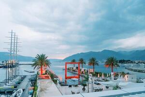 Square arch illuminated in red stands in a long pool on the pier near the moored yachts. Porto, Montenegro photo