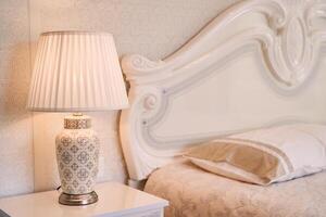 Luminous lamp with a lampshade stands near the bed on the bedside table photo