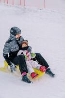 Smiling mother and little girl riding down the slope on a sleigh photo