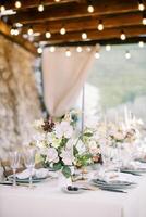 ramo de flores de flores soportes en un festivo mesa en un terraza con brillante guirnaldas foto