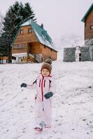 Little girl goes down a snowy hill near a wooden cottage photo