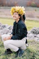 Little girl puts a wreath of autumn leaves on the head of her smiling mother sitting on a stone on the lawn photo