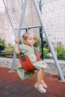 Little girl swings on a chain swing at the playground with her tongue hanging out photo