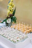 Portioned salads in cups with spoons on a tray next to mini-burgers are on the table photo