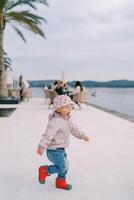 pequeño niña carreras a lo largo el terraplén por el mar, su boca abierto foto