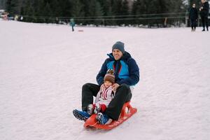 Laughing dad with a little girl sledding down a hill photo