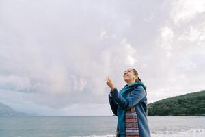 Young woman is standing by the sea with a kite spool in her hands, straightening the thread, and looking up photo