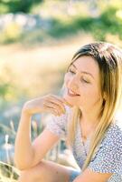 Smiling woman sitting on the grass touching her chin with her fingers photo