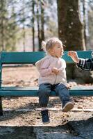 Little girl eats porridge from a spoon that her mother gives her on a bench in the forest. Cropped photo