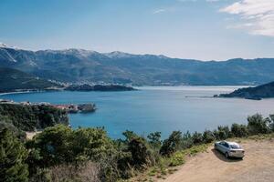 Car stands on the seashore with a view of the mountains and the old town photo