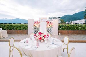 Round festive table with chairs stands opposite a stand with bouquets of flowers. Caption. Love forever photo