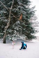 Little girl and dad making snowballs in a snowy forest photo
