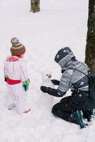pequeño niña mira a un monigote de nieve hecho por su madre en el bosque foto