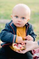 Little boy picks out pomegranate seeds from his mother palm while sitting on a blanket in the park. Cropped photo