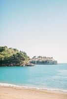 View from the sandy beach of the island of Sveti Stefan, looking out from behind a wooded cliff. Montenegro photo